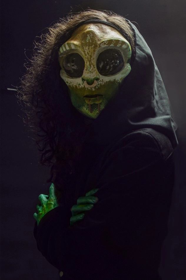Anki from Losaquis crossing her arms under low light during an alien ritual performance evoking mystery and ancestral alien presence